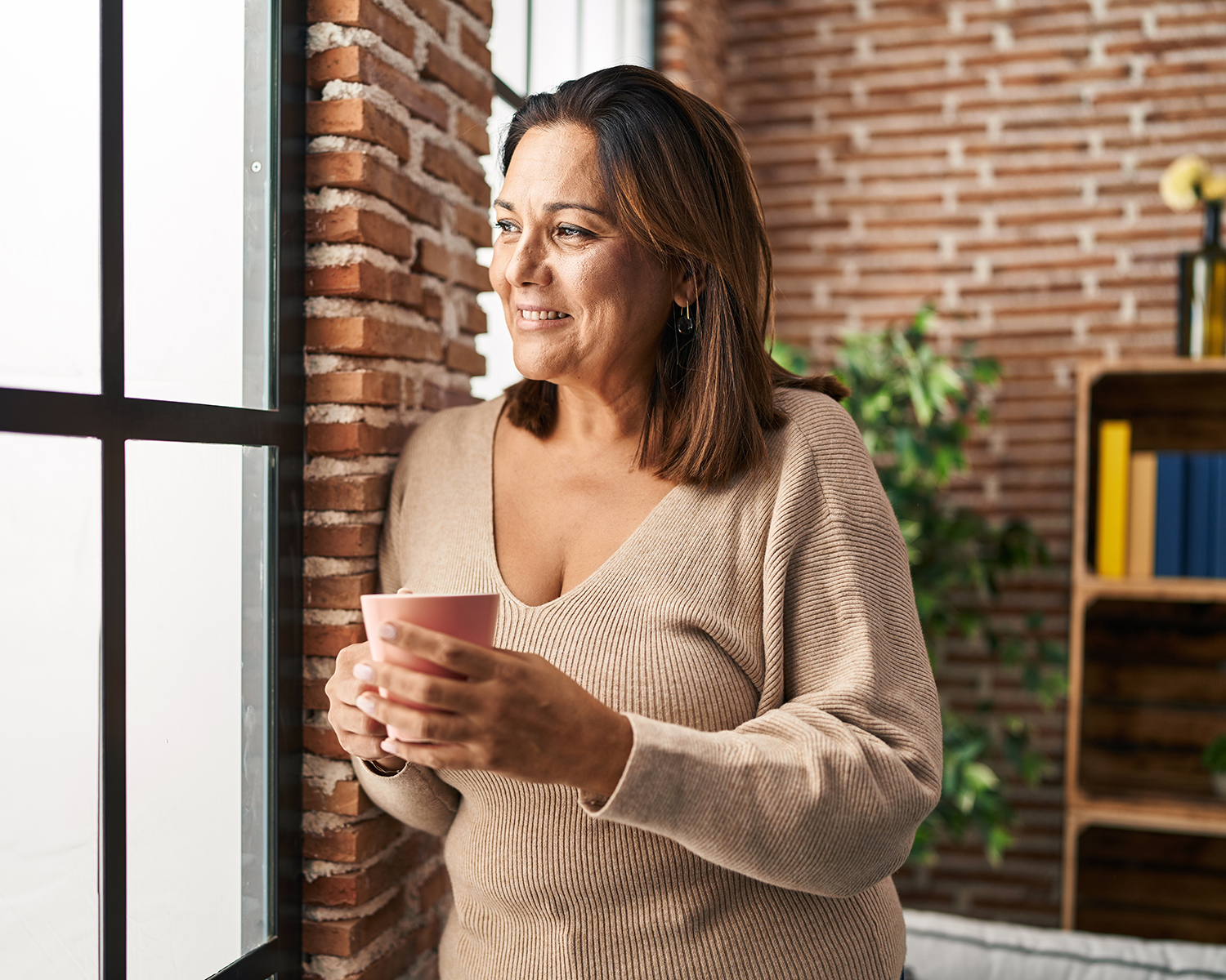 Older woman looking out a window holding coffee mug