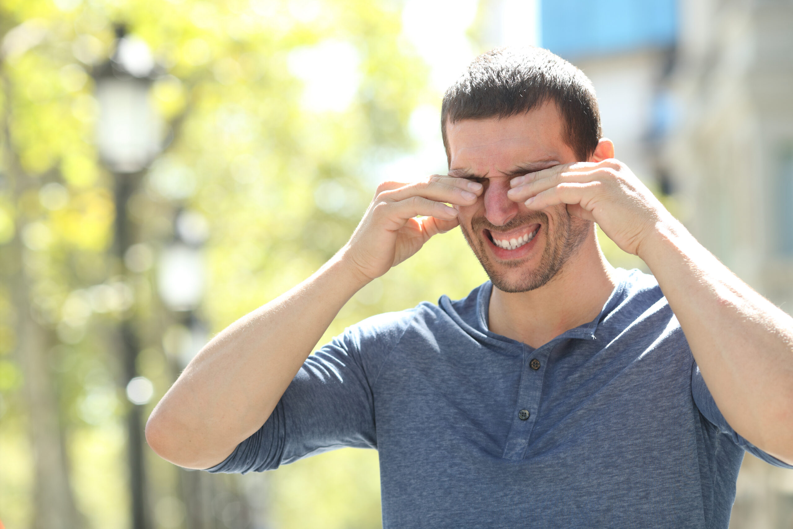 Adult man scratching itchy eyes with both hands standing in the street