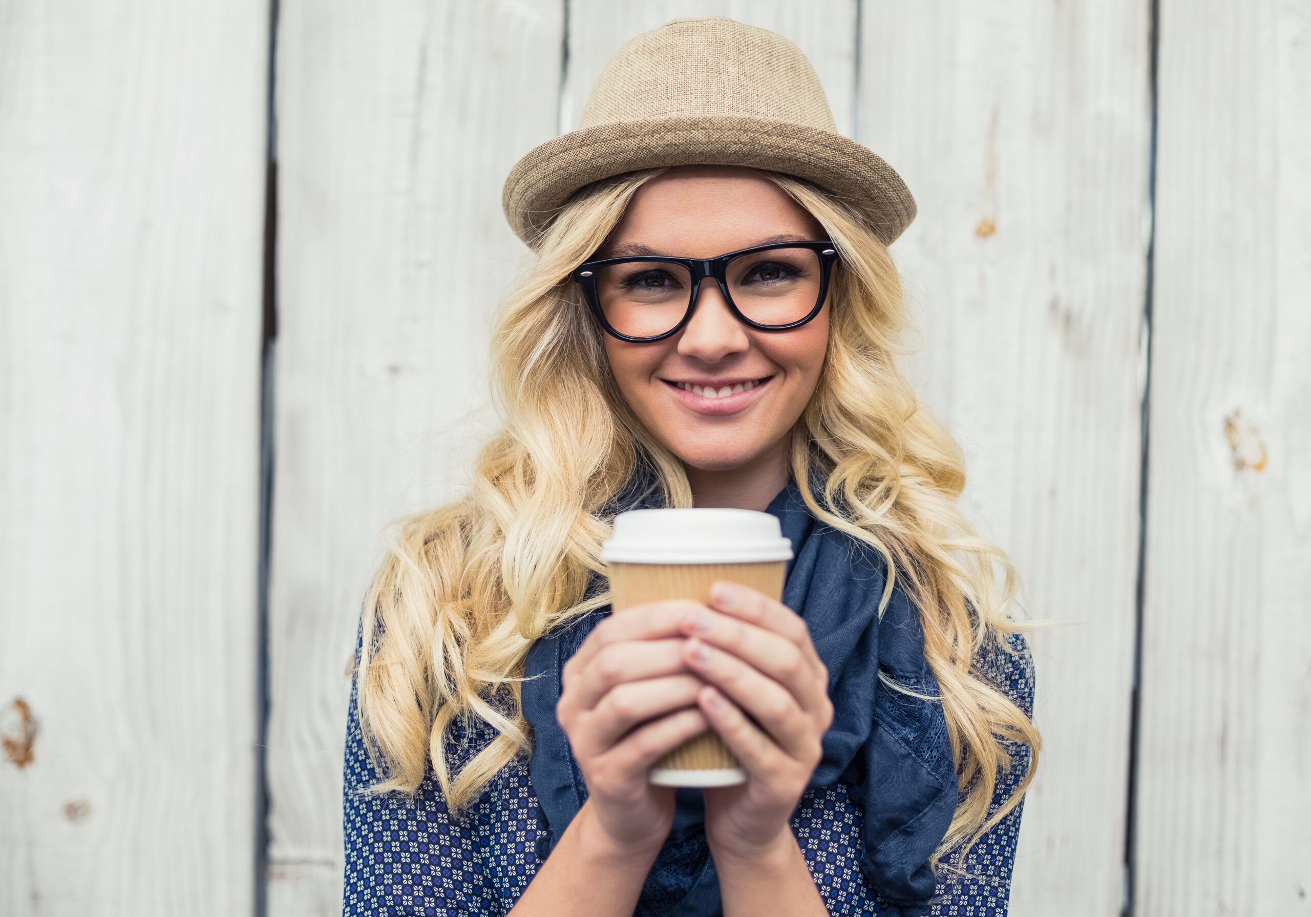 Cheerful fashionable blonde holding coffee outdoors on wooden background