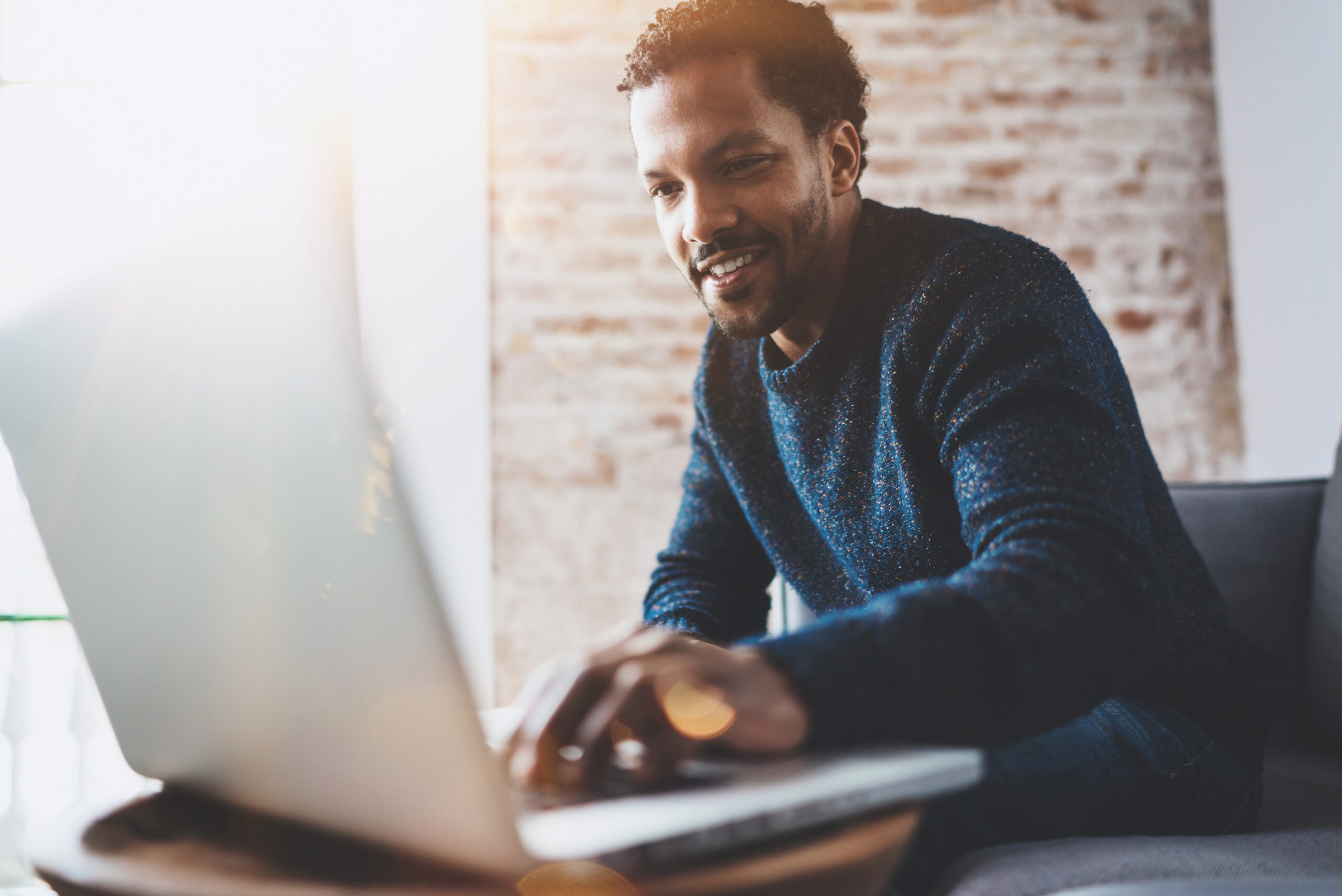 man using computer and smiling while sitting on the sofa