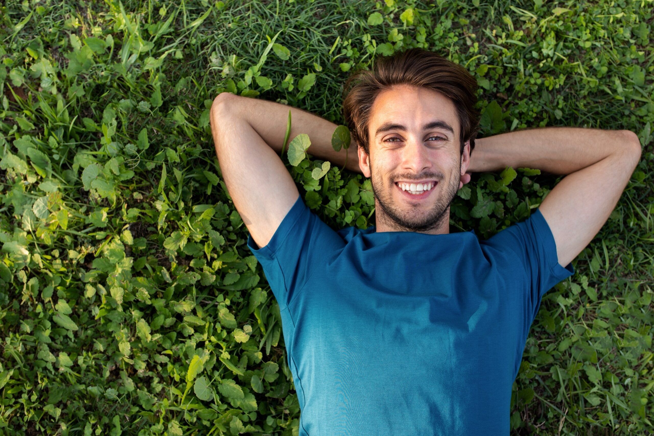 Top view of happy smiling young man relaxing lying on grass looking at camera.